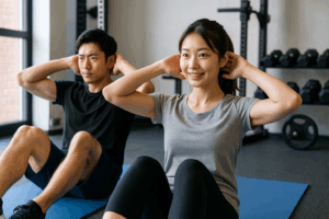 清潔感のあるジムで、日本人の男女がマットの上で腹筋トレーニングをしている様子。初心者でも取り組みやすい明るい雰囲気のリアル写真風画像。